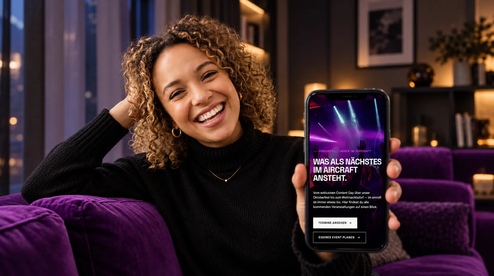 Lachende Frau zeigt die Event-Seite des aircraft events hotel auf dem Smartphone